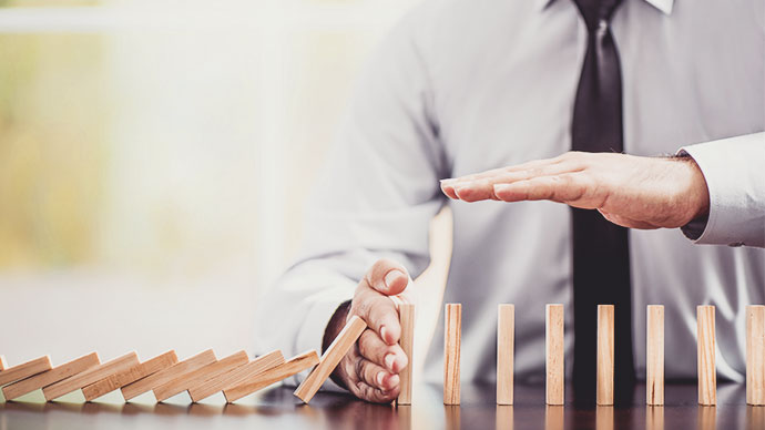 Man uses hand to stop row of falling dominos.