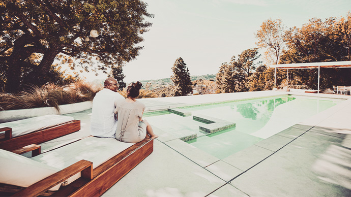 Mature couple sitting by a swimming pool.