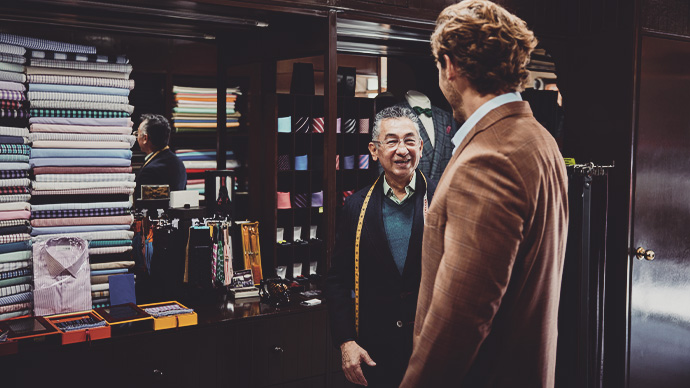 Medium wide shot of smiling tailor discussing fit of custom sportscoat with client in workshop
