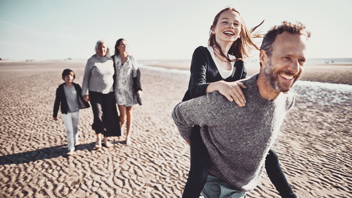 Happy father carrying daughter piggyback on the beach