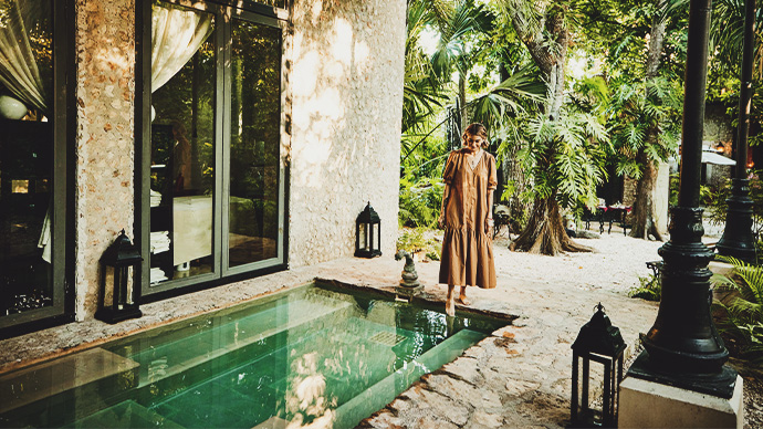 Wide shot of smiling woman standing by plunge pool at luxury tropical spa