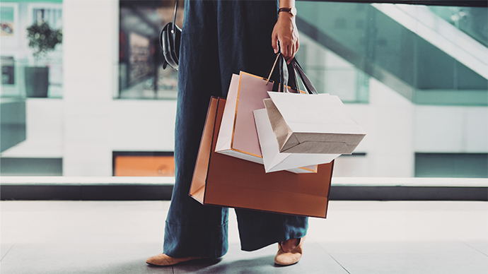 An unrecognizable Caucasian female standing at the shopping mall with paper bags.
