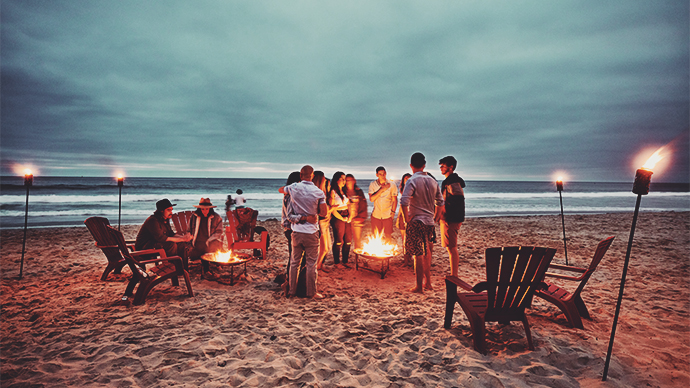 Friends gathered around fire on beach on summer evening