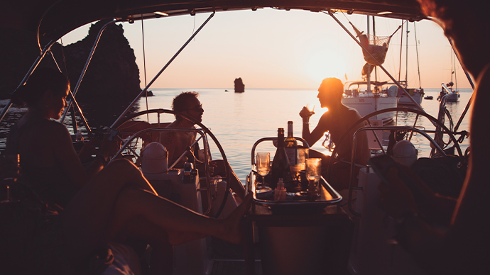 Group of friends on a sailboat, enjoying a glass of wine at sunset