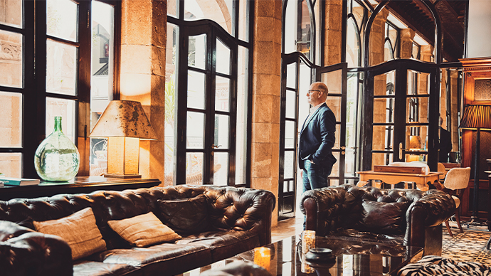 Wide shot of senior businessman looking out window in lounge of luxury hotel while on business trip
