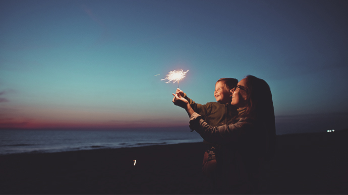 Happy little boy looking at sparkler with his parent near the sea