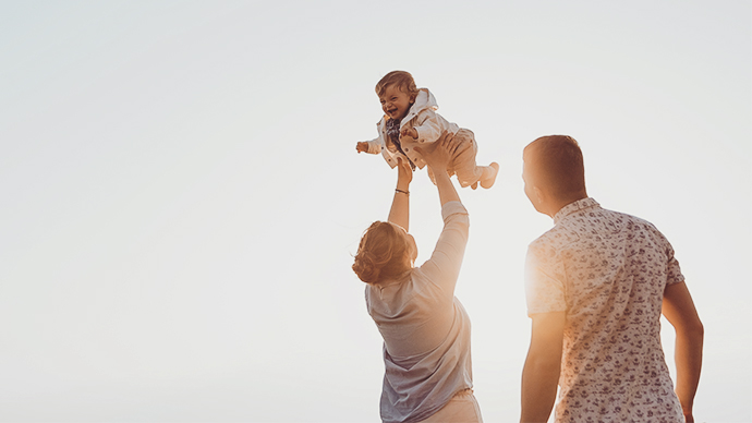 Couple with infant child, mother holding baby up in air