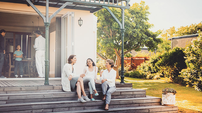 A photo of happy family relaxing at home. Females are sitting on steps and males are standing at entrance. They are in casuals.