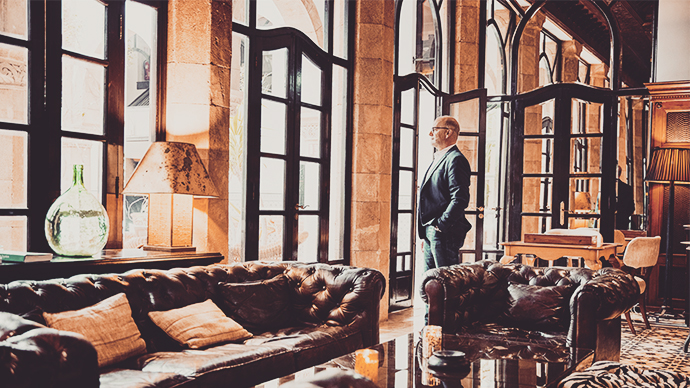 2196396161-Wide shot of senior businessman looking out window in lounge of luxury hotel while on business trip