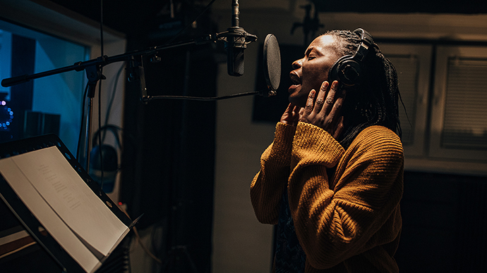 One woman, beautiful black female vocalist wearing headphones and singing into microphone in recording studio.