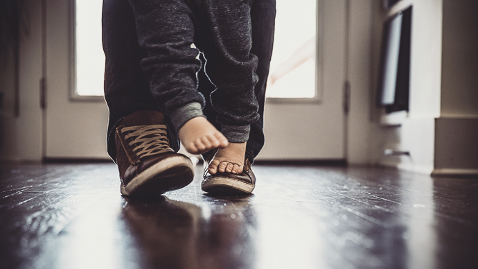 Toddler boy (2 yrs) walking on father's feet, closeup