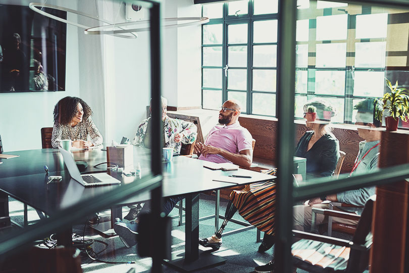 View through glass doorway into business meeting, multi racial group of colleagues sitting and discussing