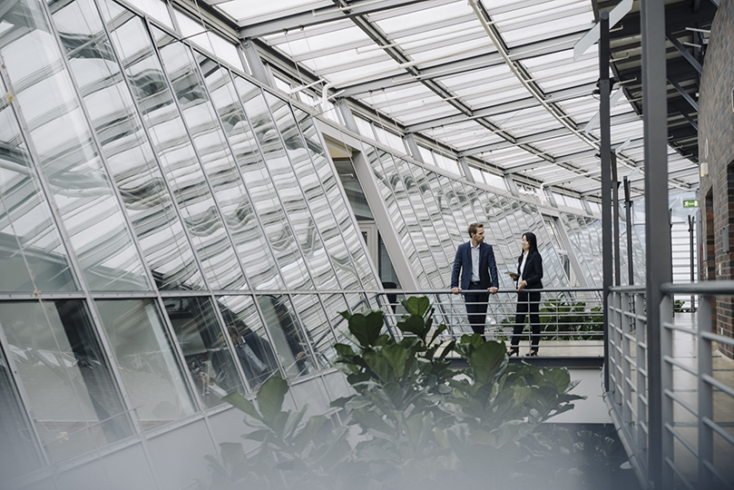 Businessman and businesswoman standing on a skywalk in modern office building