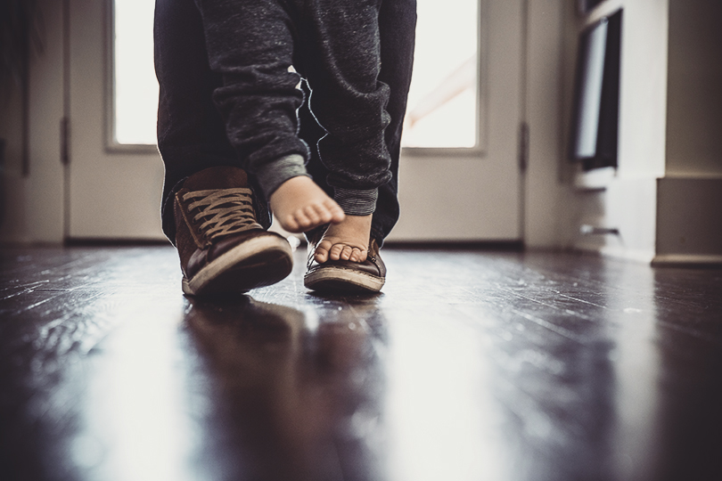 Toddler boy (2 yrs) walking on father's feet, closeup