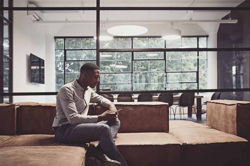 Whole Player Male entrepreneur using smart phone while sitting on sofa at workplace