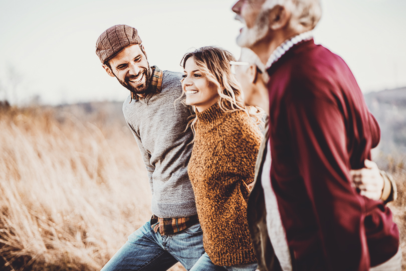 Happy couples talking while walking embraced in autumn day on the field.