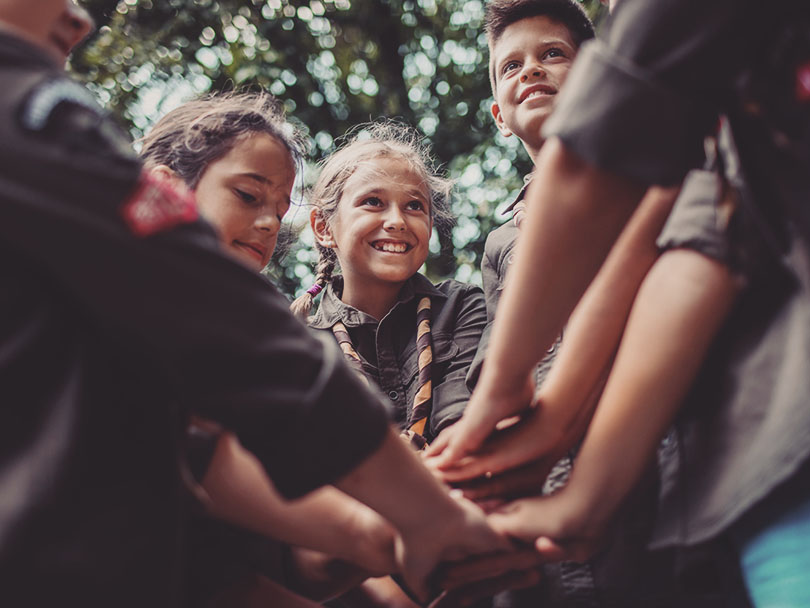 Group of young scouts joining hands together, showing their unity.