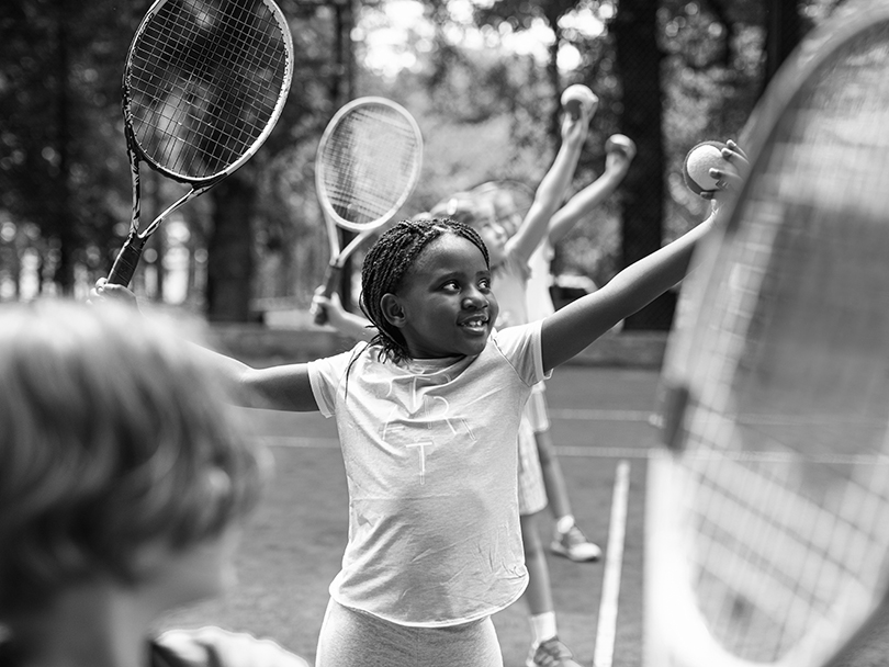 Close up of a group of kids on a tennis court learning how to serve