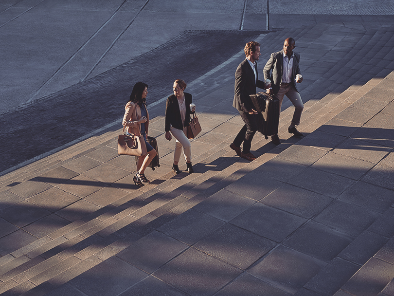 Businesspeople walking with bags on staircase outside, at sunrise