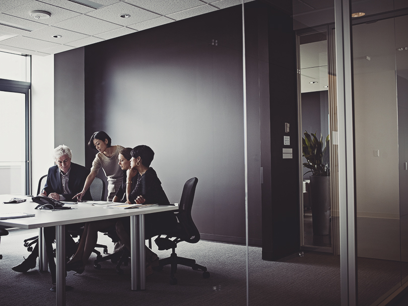 Group of coworkers in discussion in glass walled office conference room businesswoman working on digital table