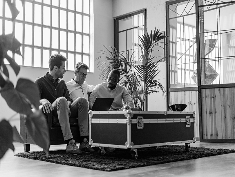 Three businessmen using laptop sitting on sofa in loft office