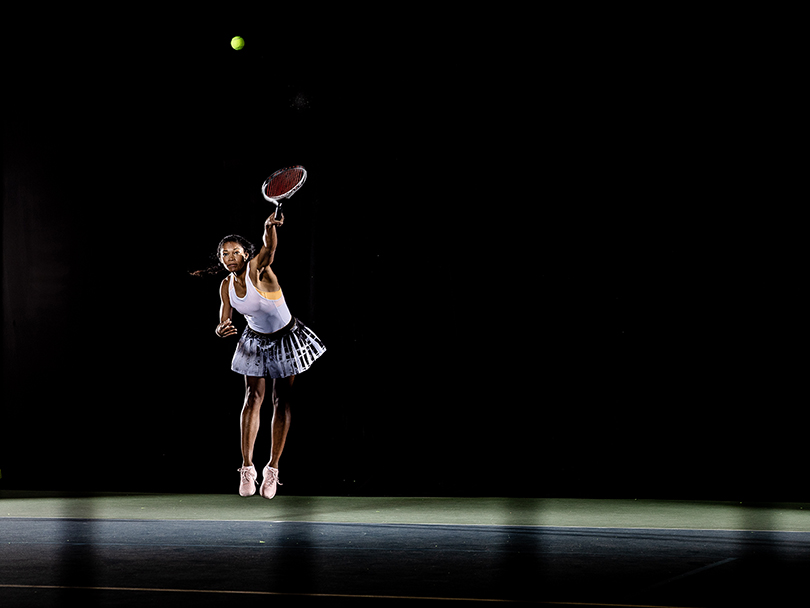 Female black tennis player hitting a serve during a tennis match, shot against a black back drop, March 3rd 2020.