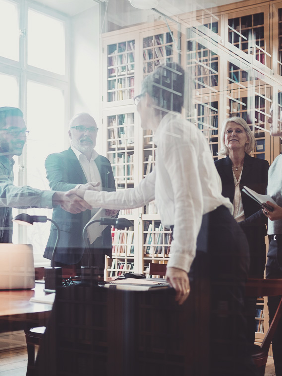 Smiling lawyers shaking hands in board room seen through glass