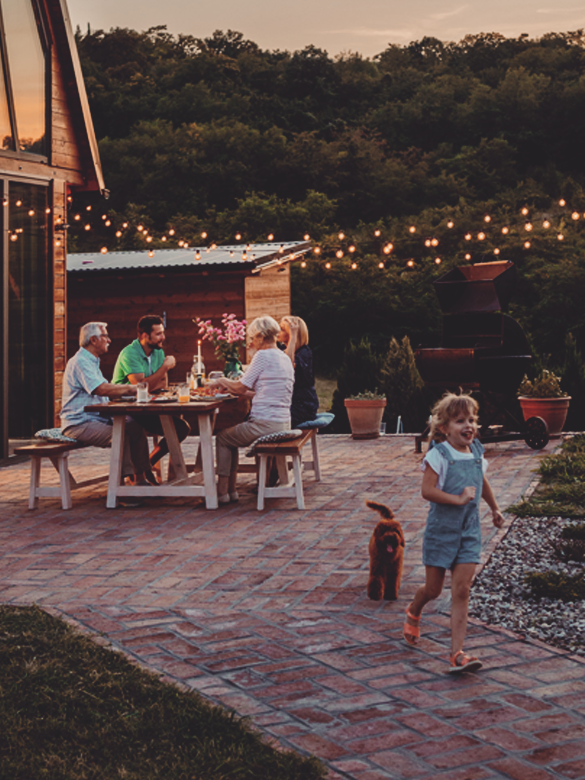 Little girl playing with her dog in the backyard while her family sitting at the dining table