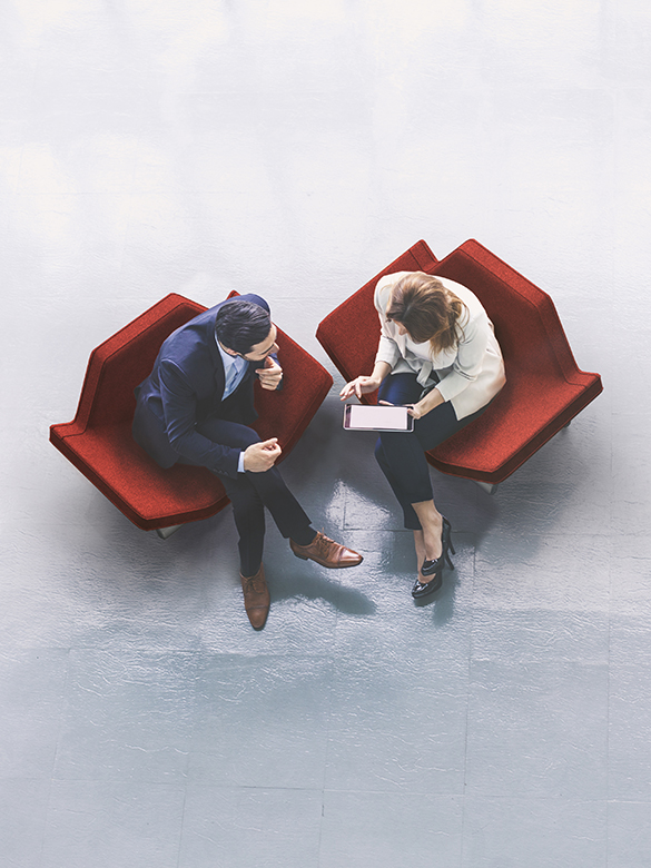 A high-angle view of a businessman and a businesswoman sitting in the office building lobby and using a tablet computer