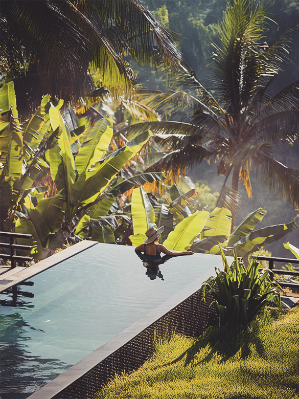 GettyImages-2150665628_Mature fit Asian woman relaxing on edge of infinity pool, admiring jungle view with early morning mist