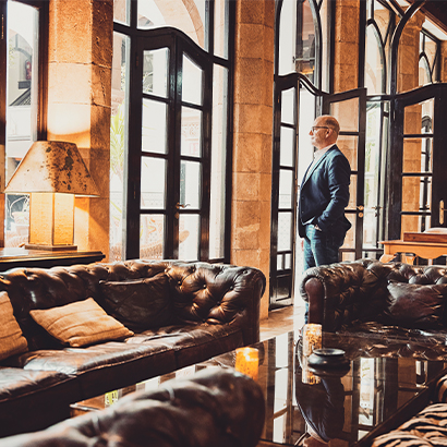 2196396161-Wide shot of senior businessman looking out window in lounge of luxury hotel while on business trip